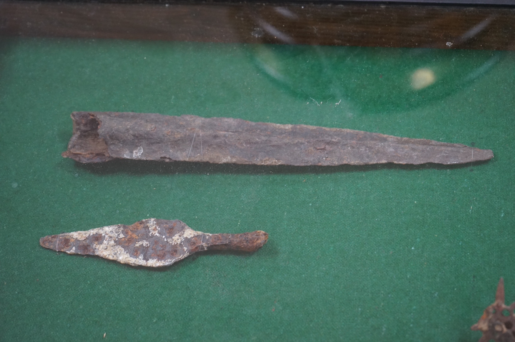 A display cabinet with a collection of antiquities comprising; medieval spur, spear and arrow heads, 53cm high. Condition - fair, relic condition